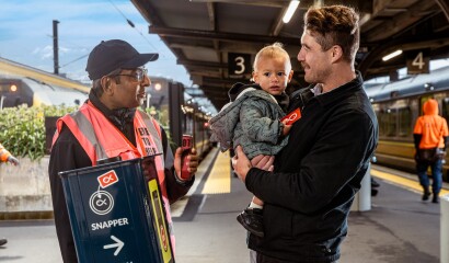 A man holding a baby talks to a Metlink staff member at Wellington Railway Station