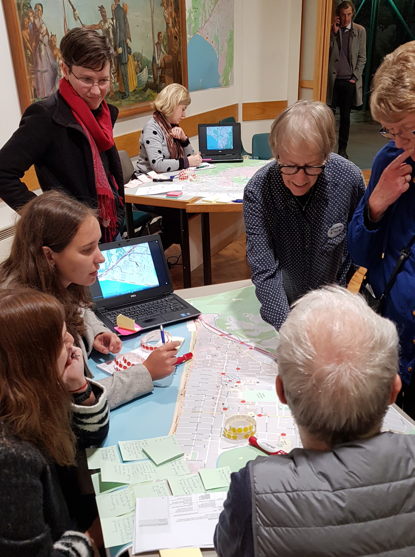 Half a dozen people stand around a table with post-its and a map during a tsunami workshop